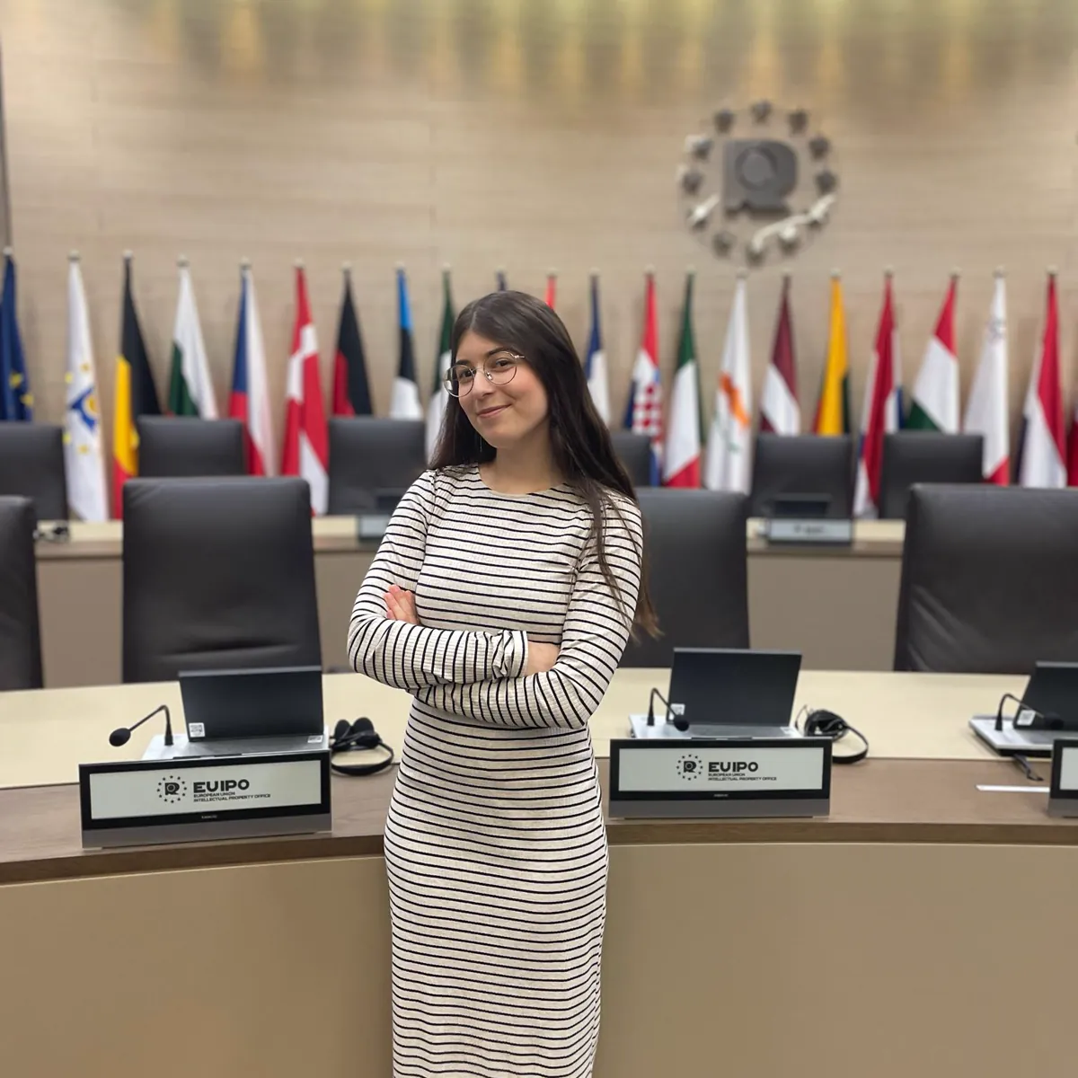 Raquel Ribera con los brazos cruzados en la sala de reuniones de la EUIPO, junto a las banderas de la Unión Europea